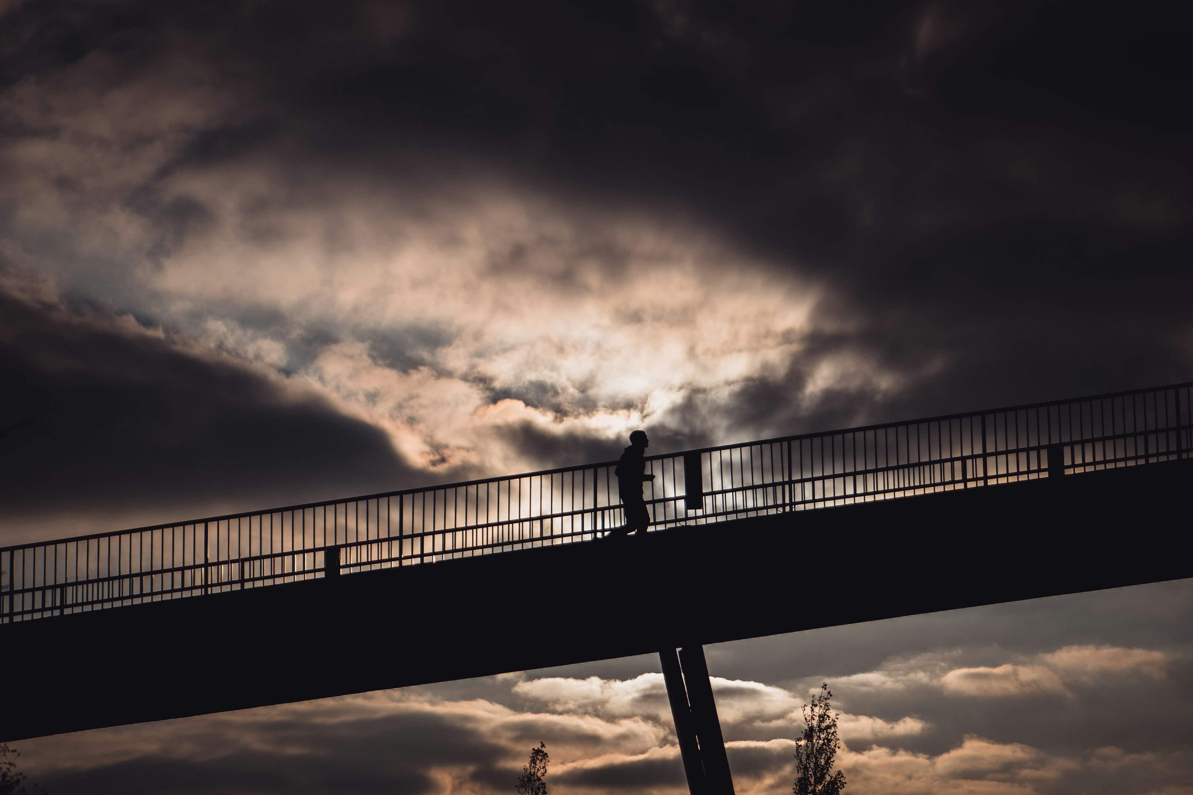 silhouette of person standing on bridge during sunset